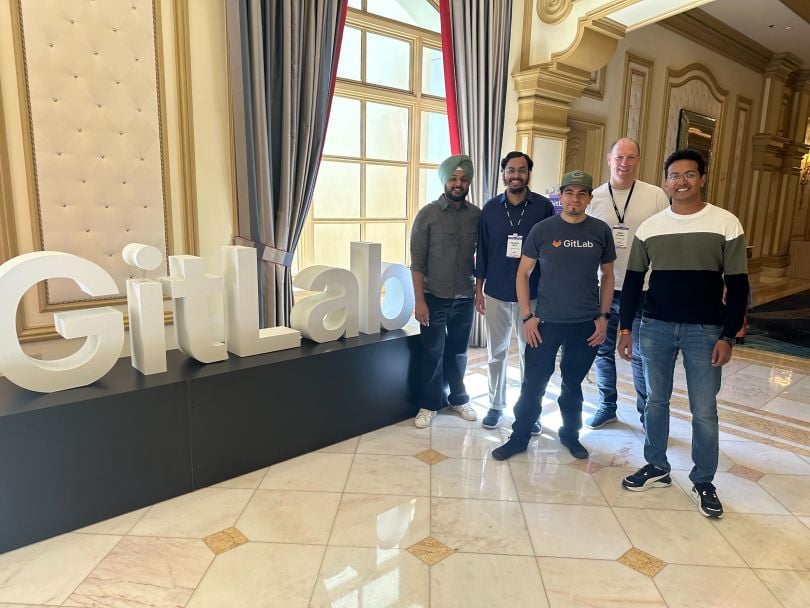 Five GitLab team members pose for a group photo beside a GitLab logo display during the company’s annual summit